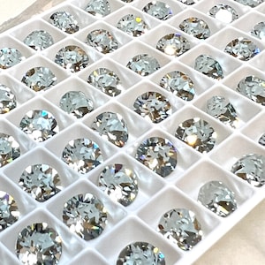 May include: A close-up view of a white plastic tray filled with clear round rhinestones. The rhinestones are arranged in rows and columns, and they are all the same size.