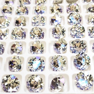 May include: A close-up view of a white plastic tray filled with clear, round, faceted rhinestones. The rhinestones are arranged in rows and columns, and they sparkle in the light.