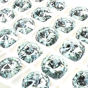 May include: A close-up view of a tray of round, clear, faceted gemstones. The gemstones are arranged in a grid pattern and have a light green hue.