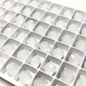 May include: A white plastic tray filled with small, round, iridescent white rhinestones.