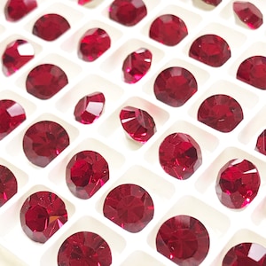 May include: A close-up view of a white tray filled with small, round, red rhinestones. The rhinestones are arranged in a grid pattern.