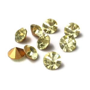 May include: A group of eight light yellow glass rhinestones with a gold-coloured metal rhinestone in the centre.