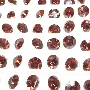 May include: A close-up view of a tray of small, round, dark red rhinestones. The rhinestones are arranged in a grid pattern.