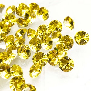 May include: A scattering of bright yellow round rhinestones on a white background.