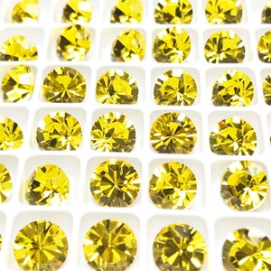 May include: A tray of round, faceted, yellow gemstones. The gemstones are arranged in a grid pattern and are all the same size.