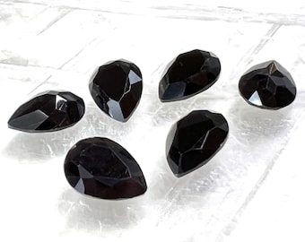 May include: Six black pear-shaped gemstones on a white background.