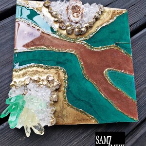 May include: A square resin art piece with a green, gold, and brown abstract design. The piece is decorated with clear and green crystals.