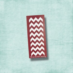 Puede incluir: Marcapáginas rectangular con borde burdeos y patrón de zigzag blanco. El texto "@mysecret.vanity" está en la esquina inferior derecha. El fondo es azul claro con escritura.