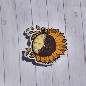 May include: A sticker featuring a yellow sunflower with a clock face inside. The clock face is partially obscured by the sunflower petals. The clock face has Roman numerals and a blue hand.