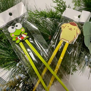 May include: Two pairs of chopsticks with cartoon character toppers. One pair has a green frog topper and the other has a yellow dog topper. The chopsticks are packaged in clear plastic bags.