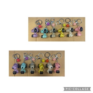 May include: Ten colorful keychains featuring a cartoon dog design. Each keychain has a silver ring and a small, colorful bead.