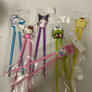 May include: Set of six colourful chopsticks with cartoon character toppers. The toppers include Hello Kitty, My Melody, Keroppi, Cinnamoroll, Kuromi, and Pompompurin.