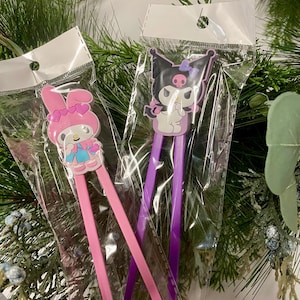 May include: Two pairs of chopsticks with cartoon character toppers. One pair is pink with a Hello Kitty character and the other pair is purple with a Kuromi character.