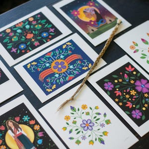 May include: A collection of eight rectangular art prints featuring diverse floral and illustrative designs on black and white backgrounds, arranged with a single braided cord placed diagonally across the centre of the display.