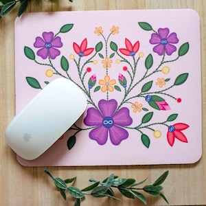 Peut inclure: Un tapis de souris rectangulaire à fond rose clair orné d'un motif floral symétrique dans des tons de violet, rouge, jaune et vert, avec de petits symboles infinis au centre des fleurs, surmonté d'une souris d'ordinateur sans fil blanche.