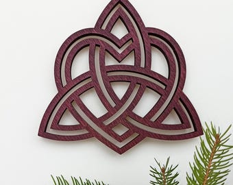 May include: A deep purple wooden wall ornament featuring an intricate, layered triquetra knot design. The cutout pattern consists of three interlocking loops forming a central triangular shape with pointed edges, showcasing a smooth, matte finish.