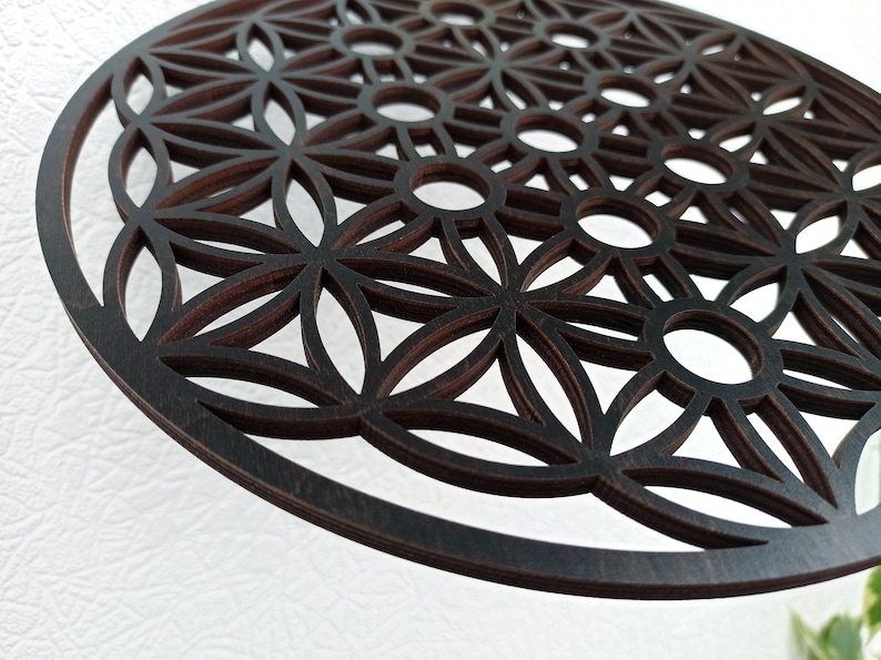May include: A dark brown wooden wall hanging with a geometric pattern of overlapping circles and flower shapes. The design is known as the Flower of Life.