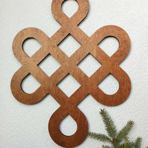 May include: A wooden wall decoration in the shape of a knot, with a brown stain finish. The knot is made of multiple overlapping circles and squares.