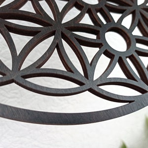 May include: A dark brown wooden mandala with a geometric pattern of overlapping circles and flower shapes. The mandala is cut out, creating a delicate and intricate design.