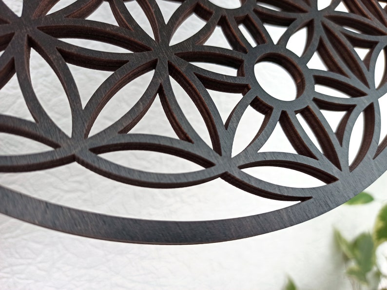 May include: A dark brown wooden mandala with a geometric pattern of overlapping circles and flower shapes. The mandala is cut out, creating a delicate and intricate design.