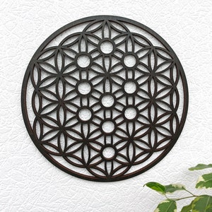 May include: A dark brown wooden wall hanging in the shape of a circle with a geometric pattern of overlapping circles and flower shapes. The pattern is known as the Flower of Life.