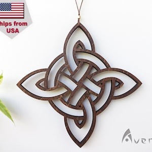 May include: A wooden Celtic knot wall hanging with a dark brown finish. The intricate design is suspended by a brown cord. The artwork is a four-pointed knot with a repeating pattern. The brand name "Averole" is visible in the bottom right corner.