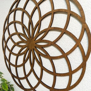K&ouml;nnte beinhalten: Eine braune Holz-Wanddekoration mit einem geometrischen Design. Das Design ist ein Kreis mit einer Reihe konzentrischer Kreise und Linien, die vom Zentrum ausstrahlen.