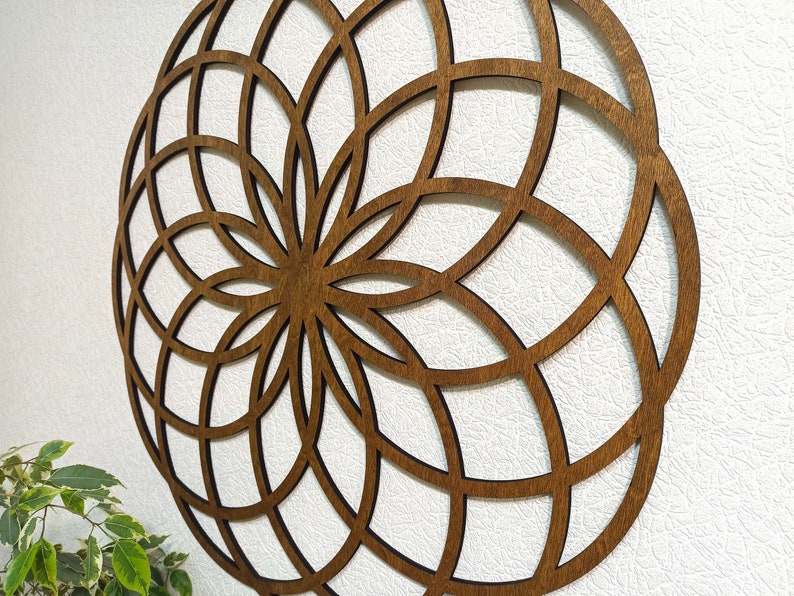 K&ouml;nnte beinhalten: Eine braune Holz-Wanddekoration mit einem geometrischen Design. Das Design ist ein Kreis mit einer Reihe konzentrischer Kreise und Linien, die vom Zentrum ausstrahlen.