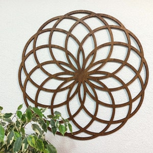 K&ouml;nnte beinhalten: Eine gro&szlig;e, runde Wanddekoration aus Holz mit einem geometrischen Muster. Das Design besteht aus einer Reihe sich &uuml;berlappender Kreise und Linien, die eine komplizierte und symmetrische Mandala-Form bilden.