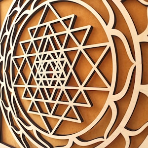 Op de afbeelding: Een houten wanddecoratie met een geometrisch ontwerp in het midden, omringd door een decoratieve rand. Het ontwerp is een Sri Yantra, een heilig symbool in het hindoe&iuml;sme.