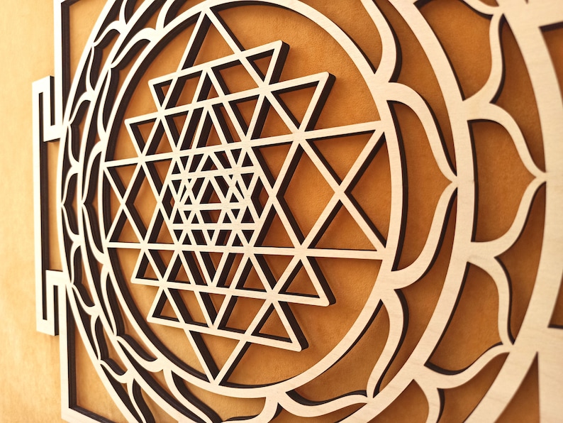 Op de afbeelding: Een houten wanddecoratie met een geometrisch ontwerp in het midden, omringd door een decoratieve rand. Het ontwerp is een Sri Yantra, een heilig symbool in het hindoe&iuml;sme.