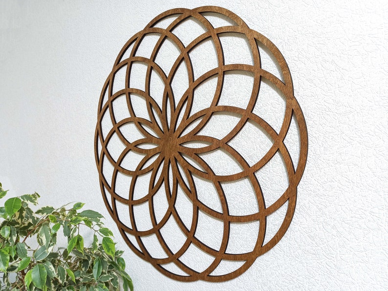 K&ouml;nnte beinhalten: Eine braune Holz-Wanddekoration mit einem geometrischen Design. Das Design ist ein Kreis mit einer Reihe konzentrischer Kreise und Linien, die vom Zentrum ausstrahlen.