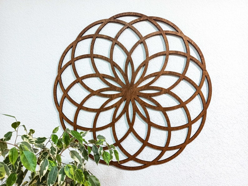 K&ouml;nnte beinhalten: Eine gro&szlig;e, h&ouml;lzerne Wanddekoration in Form eines Mandalas mit komplizierten geometrischen Mustern. Das Mandala ist braun und hat eine kreisf&ouml;rmige Form.