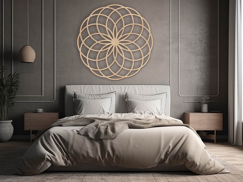K&ouml;nnte beinhalten: Eine geometrische Mandala-Wanddekoration aus Holz mit einem runden Design in einem Schlafzimmer. Das Mandala h&auml;ngt &uuml;ber einem Bett mit wei&szlig;en Bettw&auml;sche und einer braunen Wolldecke.
