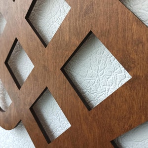 May include: A brown wooden wall decoration with a geometric design featuring a repeating pattern of squares and circles. The design is reminiscent of a Celtic knot.