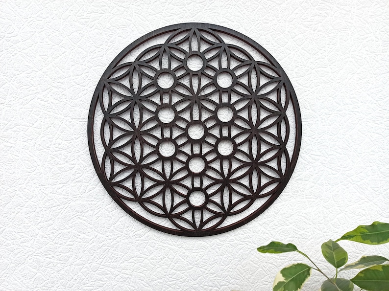 May include: A dark brown wooden wall hanging in the shape of a circle with a geometric pattern of overlapping circles and flower shapes. The pattern is known as the Flower of Life.
