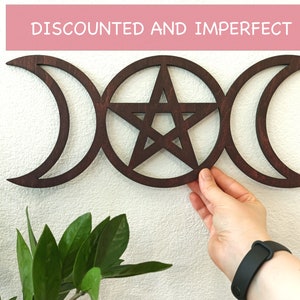May include: A dark brown wooden wall hanging with a triple moon and pentagram design. The design is a popular symbol in Wiccan and pagan traditions.