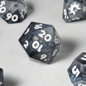 Puede incluir: Un conjunto de siete dados poliédricos de varias formas, incluyendo un d4, d6, d8, d10, d12, d20 y un dado de porcentaje. Los dados son de color gris y negro veteado con números y símbolos blancos. Ideal para juegos de mesa.