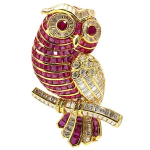 Peut inclure: Broche en forme de hibou doré, ornée de rubis et de diamants. Le hibou est perché sur une branche, avec des rubis formant le corps et des diamants soulignant les ailes et la branche. Les yeux sont en rubis.