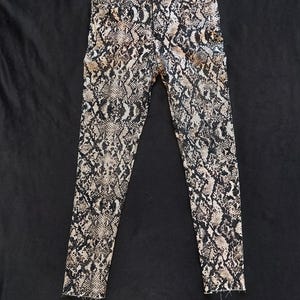 May include: Black and white snake print skinny jeans. The jeans have a dark wash and a distressed hem.