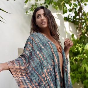 May include: A flowing, open-front kimono in shades of teal and tan. The fabric features a tie-dye pattern with vertical stripes. The garment is lightweight and appears to be made of a soft material, suitable for warm weather.