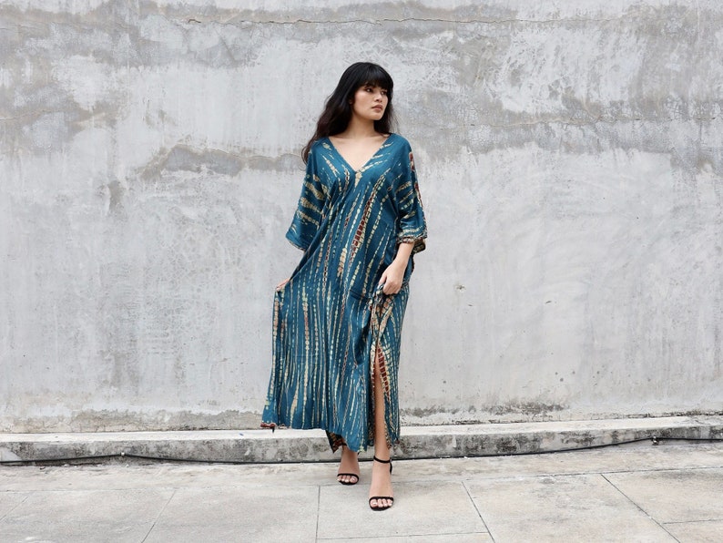 May include: A teal blue maxi dress with a tie-dye pattern and a side slit. The dress has a V-neck and 3/4 sleeves.