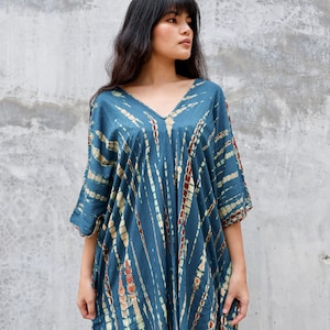 May include: A blue and white tie-dye kaftan dress with a V-neckline. The dress has a loose, flowing fit and is perfect for a casual summer look.