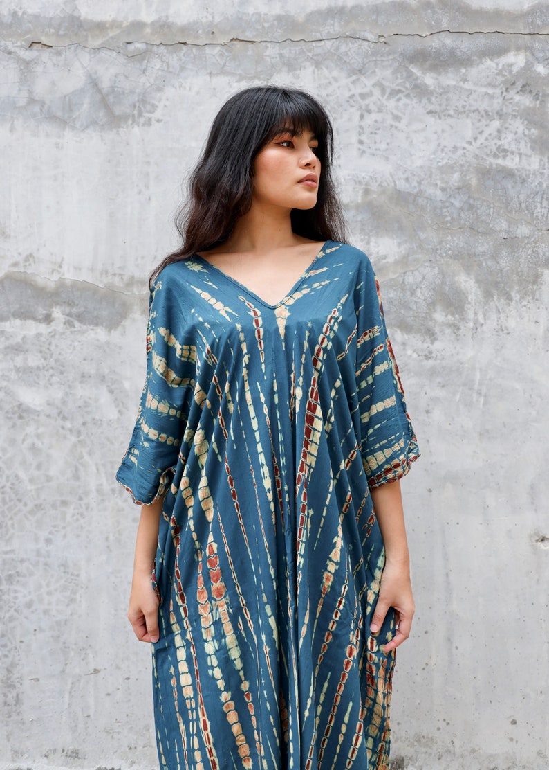 May include: A blue and white tie-dye kaftan dress with a V-neckline. The dress has a loose, flowing fit and is perfect for a casual summer look.
