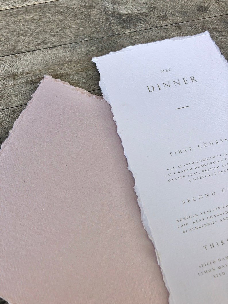 May include: A close-up of a dinner menu and a pink paper. The menu is white with the word "DINNER" in a dark gray font. The menu has a torn edge. The pink paper has a torn edge.