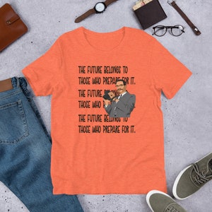 Puede incluir: Camiseta naranja con una imagen en blanco y negro de un hombre sosteniendo una c&aacute;mara. El texto en la camiseta dice "The future belongs to those who prepare for it."