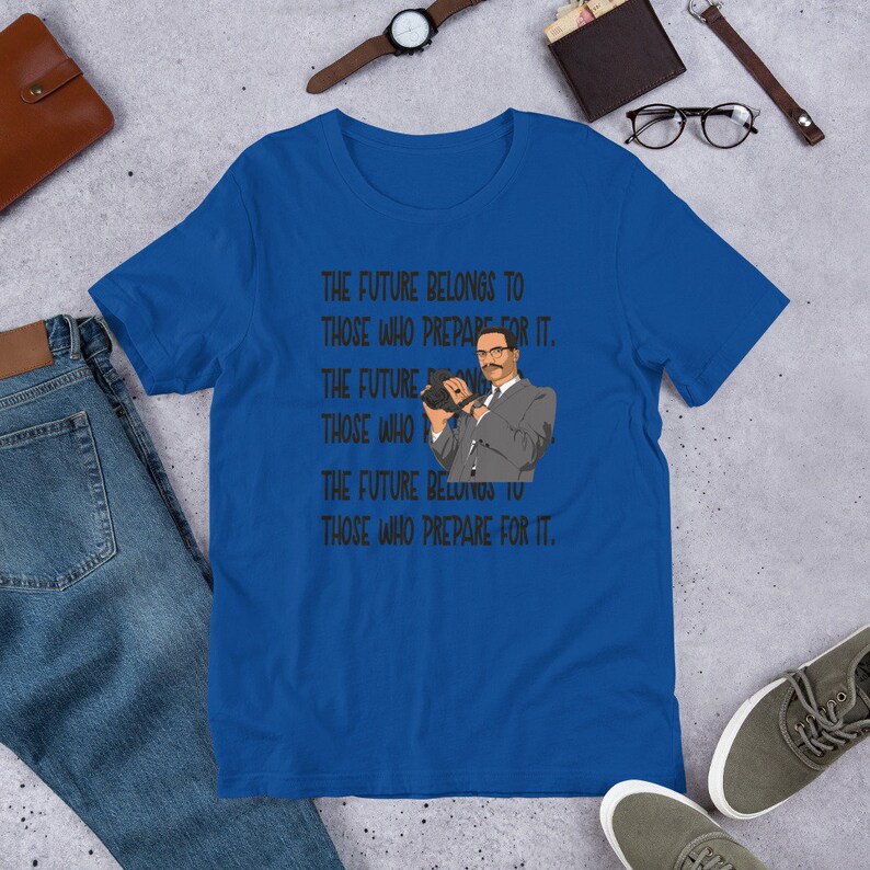 Puede incluir: Una camiseta azul real con una imagen en blanco y negro de un hombre sosteniendo una c&aacute;mara. El texto en la camiseta dice "THE FUTURE BELONGS TO THOSE WHO PREPARE FOR IT."