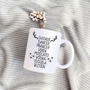 Könnte beinhalten: Weiße Keramiktasse mit einem schwarzen Rentier-Design und dem Text "Dasher Dancer Prancer Vixen Moscato Vodka Tequila Blitzen".