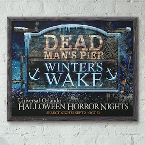 May include: A weathered wooden sign with blue and white text that reads "Dead Man's Pier Winter's Wake". The sign is framed in a dark wood frame and has a background of a dark blue and white scene. The text "Universal Orlando Halloween Horror Nights Select Nights Sept 2-Oct 31" is printed below the sign.