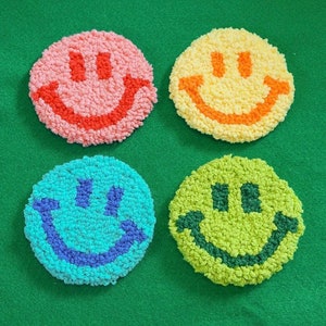 Pode incluir: Quatro patches de carinhas sorridentes coloridos com fundos de diferentes cores e contornos pretos. Os patches são feitos de fio felpudo e são perfeitos para adicionar um toque de fantasia a qualquer projeto.